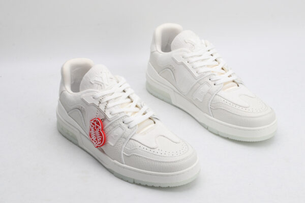 "A pair of PureEssence All-White Luxury Sneakers, viewed from an angle, showcasing their pristine low-top design, white laces, premium white leather upper with subtle textures, and a small red tag hanging from the left shoe