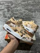 A pair of Jordan 'Desert Camo' lifestyle sneakers, displaying their camouflage pattern, white midsoles with visible Air units, and gum outsoles, resting on a beige shoe box.