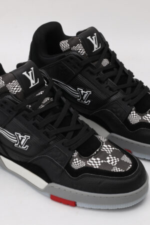 A pair of black low-top sneakers featuring white and grey checkerboard patterns on the tongue and side panels, a prominent white logo, and subtle red detailing on the sole, displayed against a light grey background.