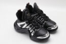 A single black chunky athletic sneaker with a large, sculptural wavy black sole, featuring reflective silver metallic overlays on the upper and black laces, displayed from a side profile against a plain white background.