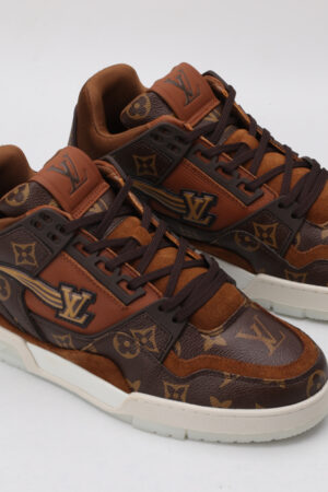 A pair of brown and tan monogrammed low-top sneakers with darker brown accents, brown laces, and a contrasting white outsole, displayed against a light grey background.
