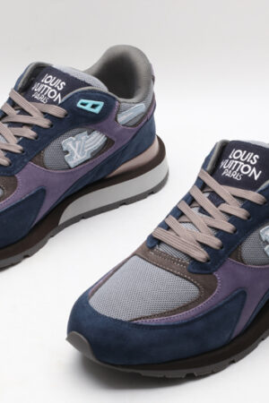 A pair of athletic sneakers in navy blue suede, purple fabric, and grey mesh, featuring taupe laces, light blue accents, and a layered brown and grey sole with branding on the side, displayed against a plain white background