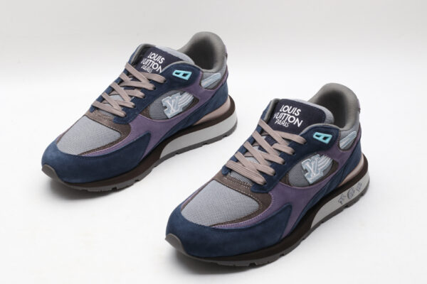 A pair of athletic sneakers in navy blue suede, purple fabric, and grey mesh, featuring taupe laces, light blue accents, and a layered brown and grey sole with branding on the side, displayed against a plain white background
