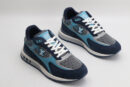 A single athletic sneaker in shades of navy blue, light blue, and grey, featuring a textured mesh upper, suede overlays, white laces, and a layered sole with iconic patterns on the side, displayed from a side angle against a plain white background.