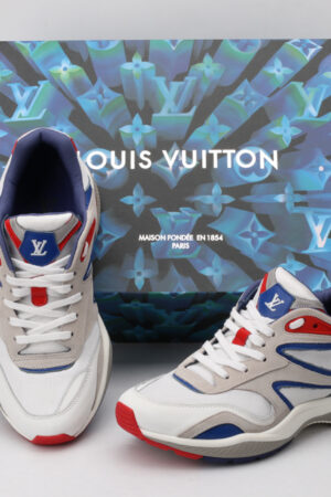A pair of white, grey, blue, and red athletic sneakers with a chunky sole, blue and red accents, a prominent blue logo on the tongue, and a visible air unit detail on the heel, displayed against a light grey background.