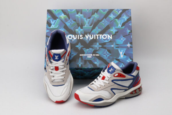 A pair of white, grey, blue, and red athletic sneakers with a chunky sole, blue and red accents, a prominent blue logo on the tongue, and a visible air unit detail on the heel, displayed against a light grey background.