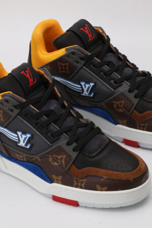 A pair of multi-toned low-top sneakers featuring brown and black monogrammed sections, vibrant blue accents on the sides, bright yellow interior lining, black laces, and a white outsole with subtle red detailing, displayed against a light grey background.