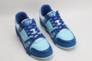 A pair of two-tone blue low-top sneakers, featuring darker blue overlays and lighter blue panels on the toe box and side, with matching blue laces, a white outsole, and intricate blue sole patterns, displayed against a light grey background.