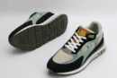 A pair of athletic sneakers in shades of forest green, earthy brown, black, and light olive mesh, featuring white laces, prominent "LOUIS VUITTON PARIS" branding on the tongue, and a layered sole, displayed from a top-down angle against a plain white background.
