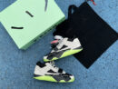 Pair of Jordan Jumpman Jack TR 'Travis Scott' sneakers in black, light grey, and neon green, showing the lateral reverse swoosh, resting on a light green surface with green plants in the background.