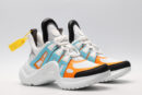 A pair of white chunky athletic sneakers with bold light blue and vibrant orange overlays, white laces, black accents on the toe and heel, and a large, sculpted white sole, displayed against a light grey background.
