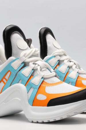 A pair of white chunky athletic sneakers with bold light blue and vibrant orange overlays, white laces, black accents on the toe and heel, and a large, sculpted white sole, displayed against a light grey background.