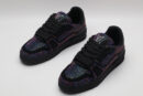 A pair of all-black Louis Vuitton LV Trainer sneakers, entirely covered in glittering multi-colored crystal embellishments, with "VUITTON" subtly visible on the side strap.