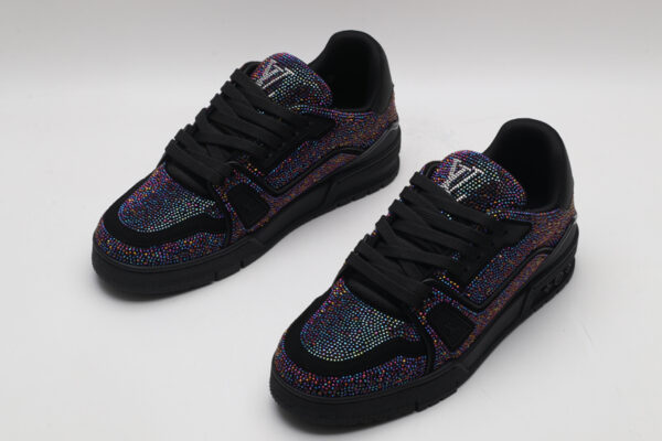 A pair of all-black Louis Vuitton LV Trainer sneakers, entirely covered in glittering multi-colored crystal embellishments, with "VUITTON" subtly visible on the side strap.
