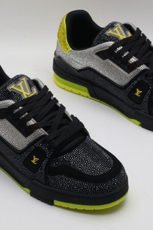 A single black and silver Louis Vuitton LV Trainer sneaker, covered in glittering silver crystal embellishments, with vibrant neon yellow accents on the heel and sole, and a prominent gold LV logo on the side.