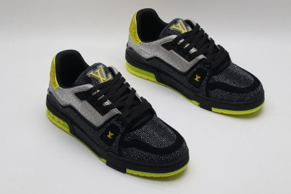 A single black and silver Louis Vuitton LV Trainer sneaker, covered in glittering silver crystal embellishments, with vibrant neon yellow accents on the heel and sole, and a prominent gold LV logo on the side.