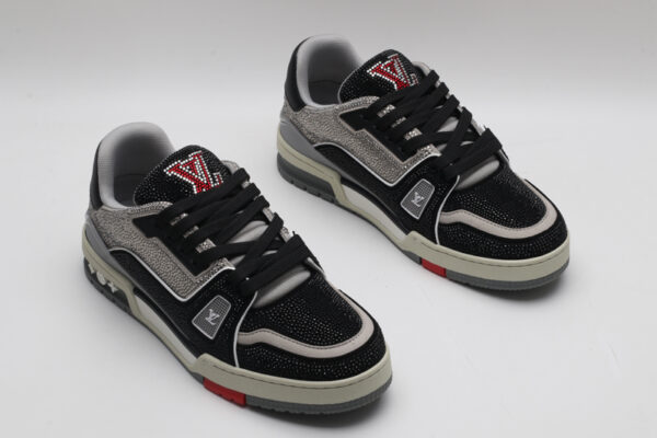 A pair of black and silver Louis Vuitton LV Trainer sneakers, entirely covered in glittering black and silver crystal embellishments, with "VUITTON" visible on the side strap