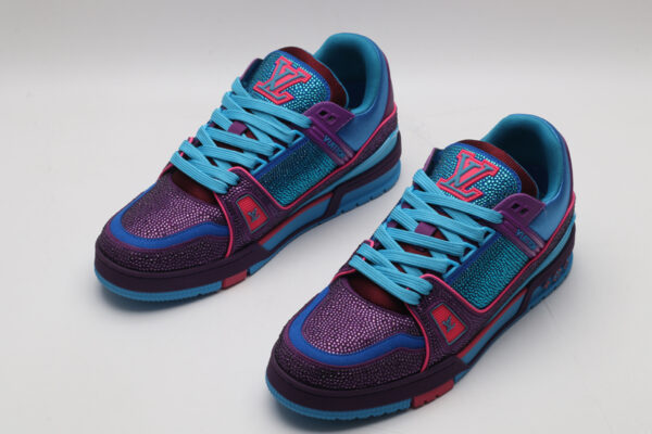 A pair of vibrant purple and blue Louis Vuitton LV Trainer sneakers, entirely covered in glittering multi-color crystal embellishments, with "VUITTON" visible on the outsole.