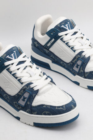 A pair of Louis Vuitton LV Trainer Low-Top Sneakers in blue denim and white, viewed from an elevated angle, showcasing both shoes with blue denim panels and white leather details.