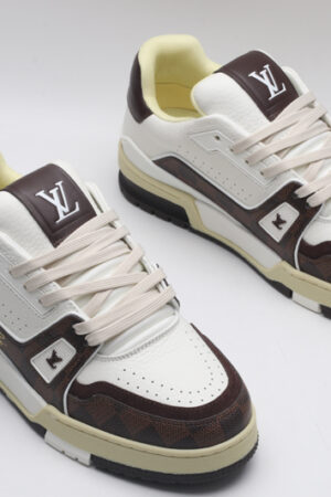 A pair of white and brown Louis Vuitton LV Trainer Low-Top Sneakers, featuring brown Louis Vuitton Monogram canvas and white leather.