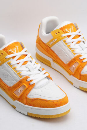 A pair of Louis Vuitton LV Trainer Low-Top Sneakers in white and orange monogram canvas, viewed from an elevated angle, showcasing both shoes with orange monogram canvas panels and white leather details.