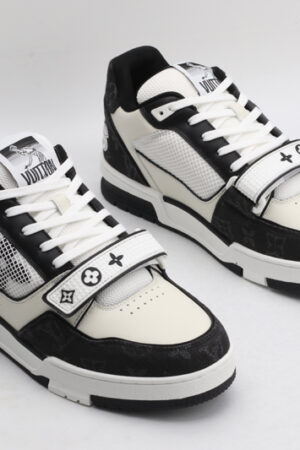 A pair of Louis Vuitton LV Trainer Mid-Top Sneakers in white and black monogram canvas, viewed from an elevated angle, showcasing both shoes with black monogram canvas panels, white and cream leather details, and a prominent white strap.