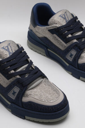 A pair of navy blue and silver Louis Vuitton LV Trainer sneakers, showcasing their bicolor design, textured panels, and robust outsole with "VUITTON" branding.