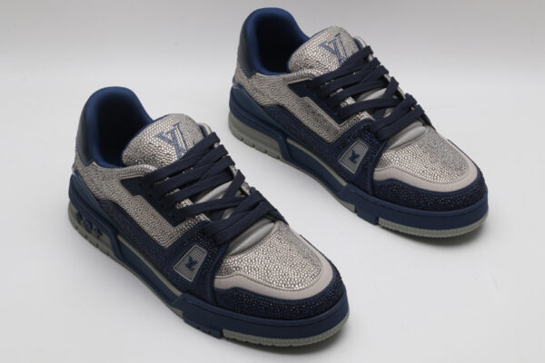 A pair of navy blue and silver Louis Vuitton LV Trainer sneakers, showcasing their bicolor design, textured panels, and robust outsole with "VUITTON" branding.