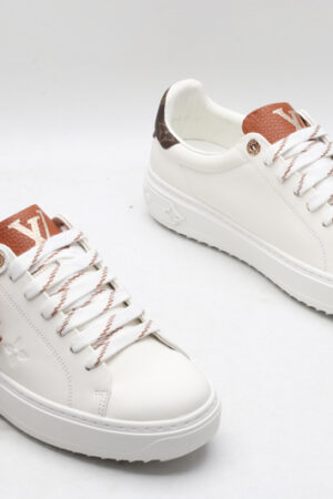 A pair of white Louis Vuitton Stellar Low-Top Sneakers with brown tongues and brown monogrammed heel tabs, one featuring a brown Louis Vuitton Monogram flower charm, viewed from a high angle.