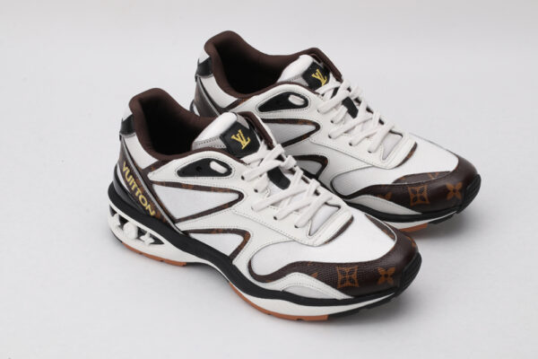 A pair of white athletic sneakers with brown monogram patterns on the toe and side, black outlining, white laces, and a multi-toned outsole with visible "VUITTON" branding on the heel, displayed against a light grey background