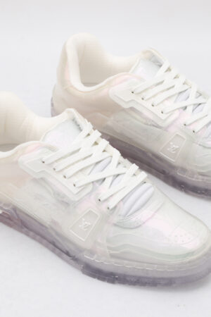A pair of luminous iridescent holographic low-top sneakers with a clear, color-shifting upper, white laces, and a textured translucent sole, presented against a pure white background