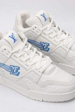 A pair of white low-top sneakers featuring a subtle all-over monogram pattern, prominent blue logos on the tongue and side with a dynamic striped effect, and white laces, set against a plain white background.