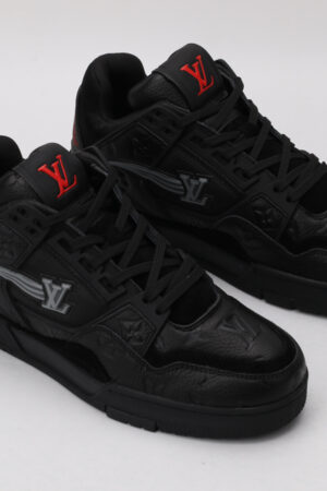 A pair of all-black low-top sneakers with textured panels, a prominent red logo on the tongue, and subtle grey detailing on the side, displayed against a light grey background.