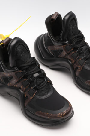 A single black and white chunky athletic sneaker with a large, sculptural wavy black sole, featuring white mesh and leather panels on the upper, black laces, and a high ankle collar, displayed from a side profile against a plain white background.