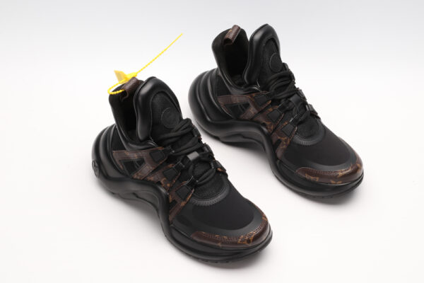 A single black and white chunky athletic sneaker with a large, sculptural wavy black sole, featuring white mesh and leather panels on the upper, black laces, and a high ankle collar, displayed from a side profile against a plain white background.