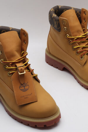 A single wheat-colored Timberland x Louis Vuitton collaborative boot, featuring a brown Louis Vuitton monogram padded collar, red-hued sole, and yellow and red laces.