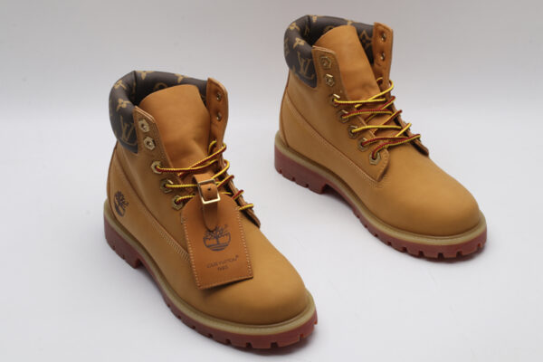 A single wheat-colored Timberland x Louis Vuitton collaborative boot, featuring a brown Louis Vuitton monogram padded collar, red-hued sole, and yellow and red laces.