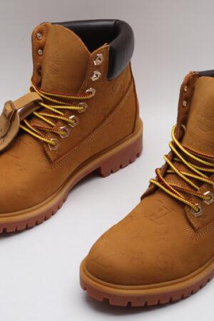 A pair of wheat-colored Timberland x Louis Vuitton collaborative waterproof boots, featuring a subtle debossed Louis Vuitton monogram, classic brown sole, and yellow and red laces