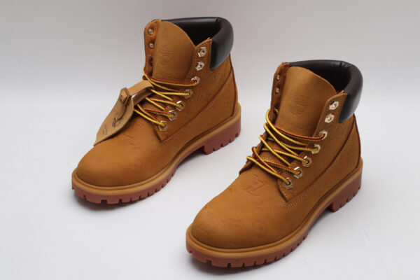 A pair of wheat-colored Timberland x Louis Vuitton collaborative waterproof boots, featuring a subtle debossed Louis Vuitton monogram, classic brown sole, and yellow and red laces
