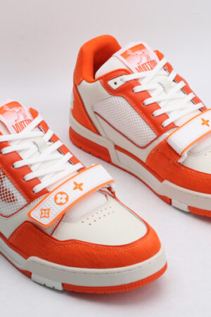 "A pair of Vibrant Horizon Orange and White Sneakers, viewed from an angle, showcasing their low-top design, white laces, orange suede accents, white leather panels, and distinctive strap across the vamp