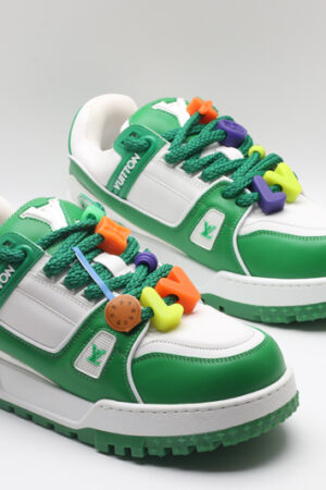 A single white and green Louis Vuitton LV Trainer Low-Top Sneaker, showcasing its full design from a slight angle, with bright orange and purple lace accents.