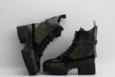 pair of dark green quilted high-top boots with black leather and suede panels, brown monogram details on the toe and base, black laces, and a chunky black lug sole, displayed against a light grey background.
