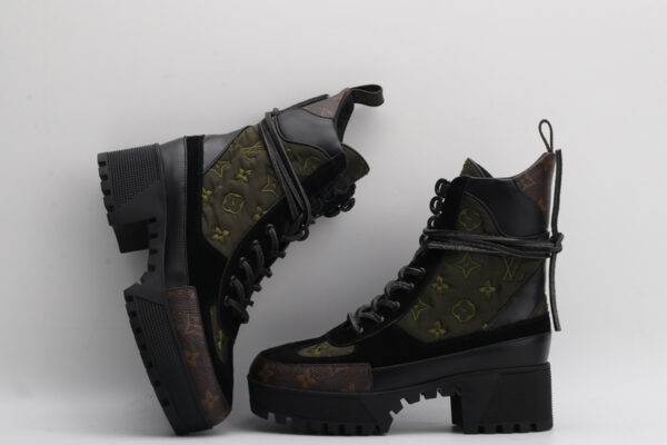 pair of dark green quilted high-top boots with black leather and suede panels, brown monogram details on the toe and base, black laces, and a chunky black lug sole, displayed against a light grey background.