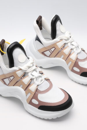 A pair of white chunky athletic sneakers with beige and light brown overlays, white laces, black accents on the toe and heel, and a large, sculpted white sole, displayed against a light grey background.