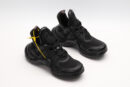 A side view of an all-black chunky sneaker. The shoe features a mix of matte leather and mesh panels, a thick, sculpted black sole, and a loop-style pull tab on the heel. The sneaker is placed on a clean, light grey background.