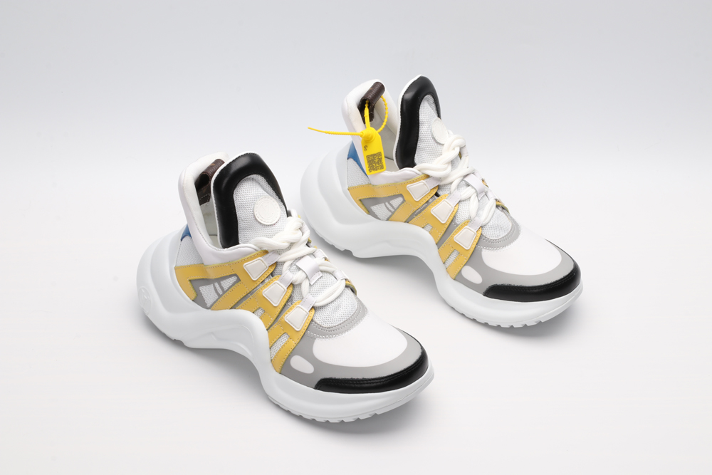 A pair of white, light blue, and black multi-panel chunky sneakers with a thick white sole, red and yellow accents, and a distinctive brown logo tag. The sneakers are photographed on a clean white background from a slightly elevated side angle.