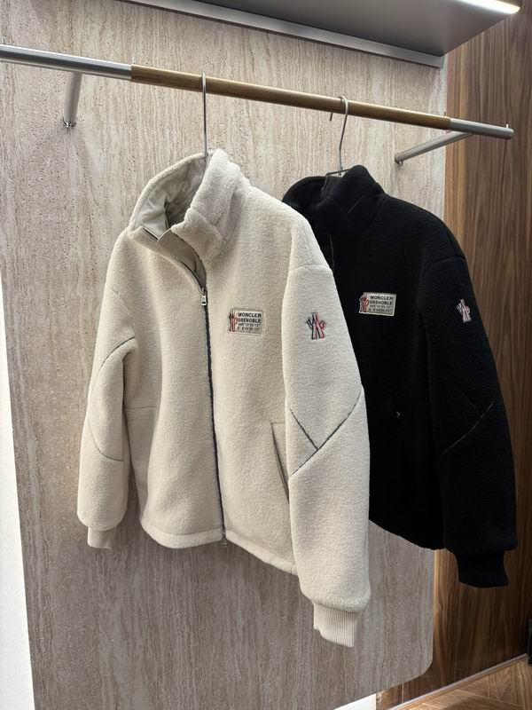 Close-up of a dark navy Moncler quilted jacket showing the brand's bell logo patch on the left shoulder and a high-quality zipper.