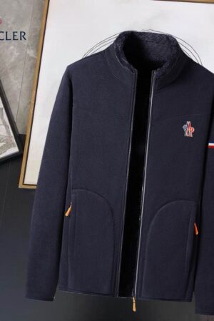 A Moncler fleece jacket in a dark color with a visible shearling lining, featuring a full zip closure and the Moncler logo patch.