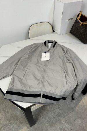 Silver or light grey Moncler nylon bomber jacket with horizontal red and blue stripes on the collar, cuffs, and hem, featuring a white Moncler logo patch on the chest