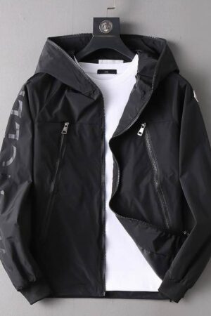 Black Moncler hooded nylon windbreaker jacket with a large, dark gray or black tonal Moncler logo print diagonally down the left sleeve